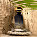 Widian Aswan bottle on stones in front of a sunlit travertine wall with a palm leaf